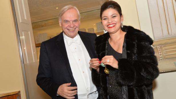 Ein Mann im Smoking und eine Frau im Pelzmantel lächeln in die Kamera.