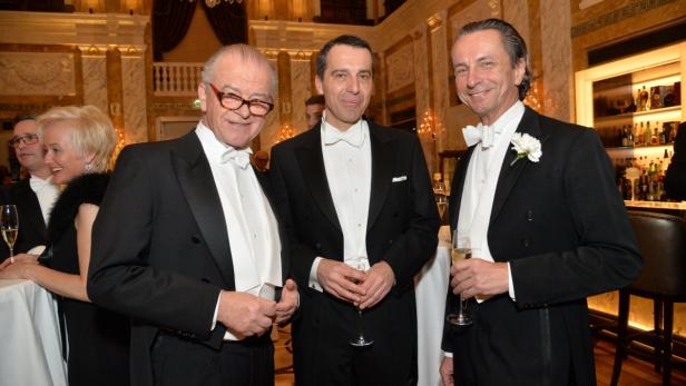 Drei Männer in Smoking stehen mit Champagnergläsern in einem eleganten Saal.