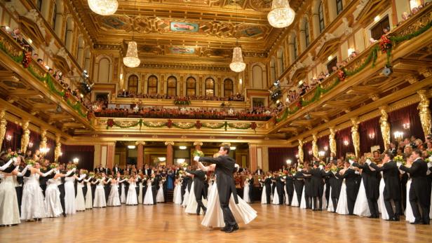 Paare tanzen in einem opulenten Ballsaal mit Zuschauern auf mehreren Ebenen.