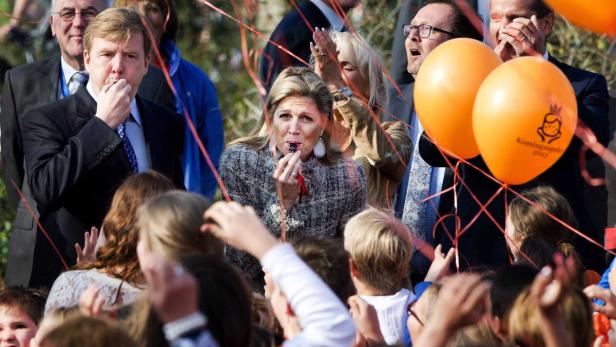 König Willem-Alexander und Königin Máxima inmitten einer Menschenmenge mit Tröten und Luftballons.