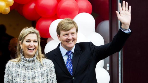 König Willem-Alexander und Königin Máxima der Niederlande winken vor einem Hintergrund aus roten und weißen Ballons.