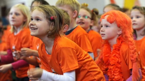 Eine Gruppe Kinder in orangefarbenen T-Shirts schaut aufmerksam in eine Richtung.