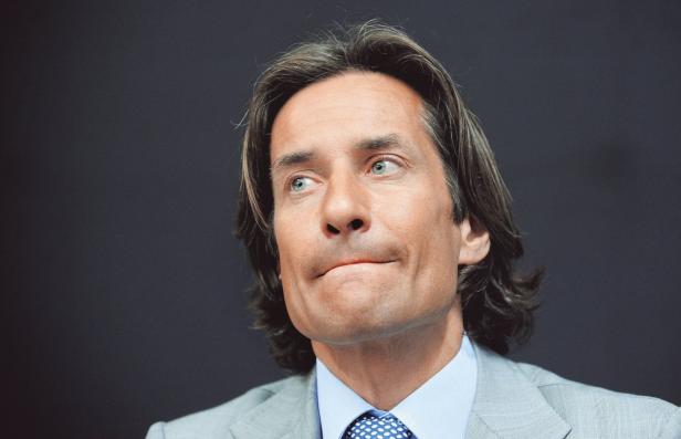 Ein Mann mit langen braunen Haaren und einem hellblauen Hemd blickt nach links.