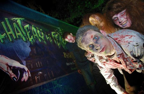 Mehrere als Zombies geschminkte Personen vor einem Banner für „Chateau of Fear“.
