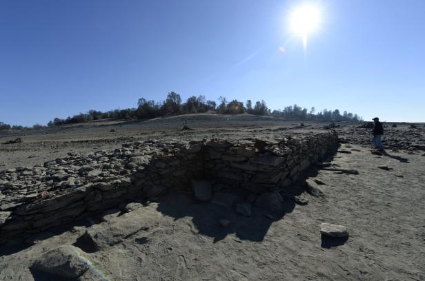 Eine Steinmauer steht in einer trockenen, sonnenbeschienenen Landschaft.