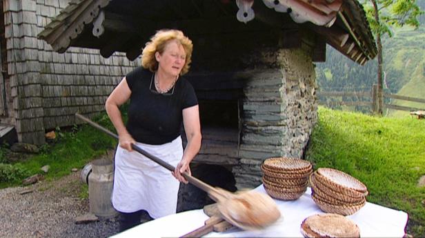 Eine Frau schiebt mit einem Brotschieber Brot in einen Steinofen.