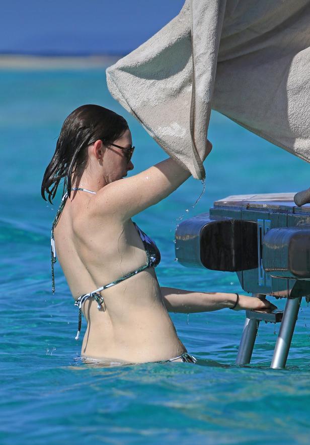 Eine Frau im Bikini steht im türkisfarbenen Wasser und hält ein Handtuch.