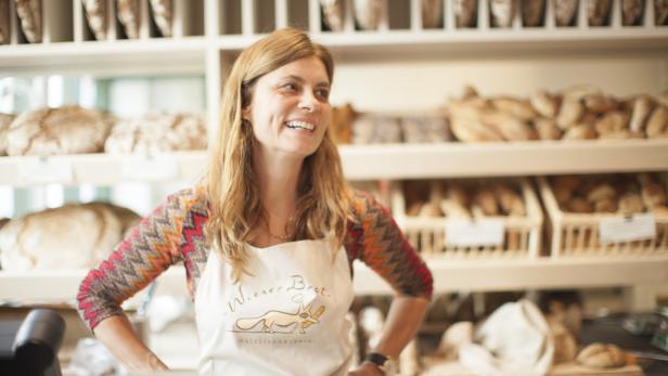 Eine lächelnde Frau steht in einer Bäckerei vor Regalen mit Brot.
