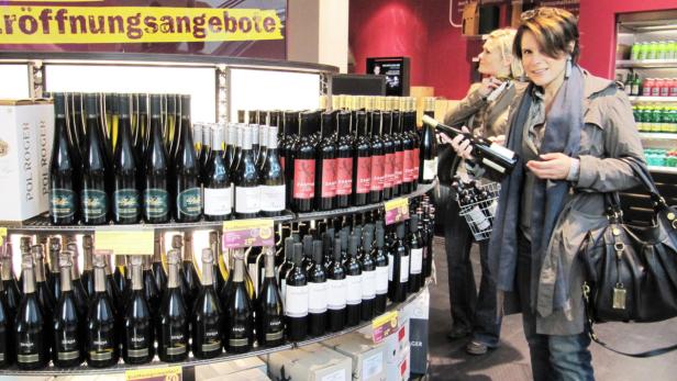 Eine Frau betrachtet eine Flasche Wein in einem Geschäft mit Weinregalen.