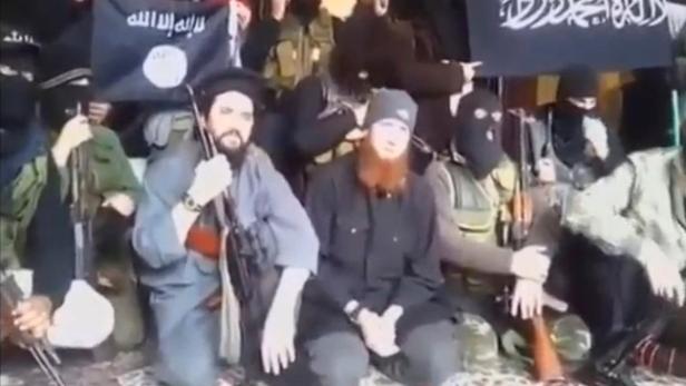 Eine Gruppe bewaffneter Männer posiert mit Flaggen, die islamische Schriftzeichen tragen.