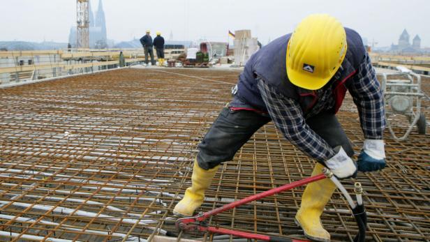 Ein Bauarbeiter mit gelbem Helm und Gummistiefeln arbeitet auf einer Baustelle mit Stahlbewehrung.
