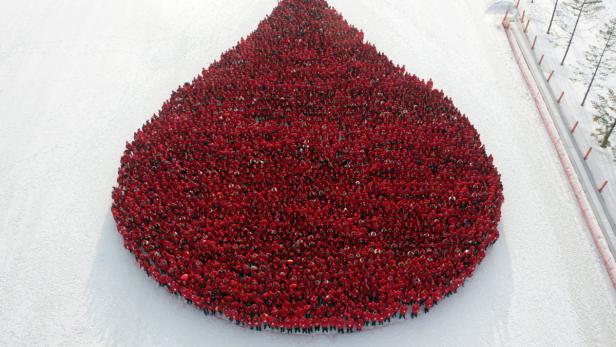 Eine große Gruppe von Menschen in roter Kleidung formt eine Blutstropfenform im Schnee.