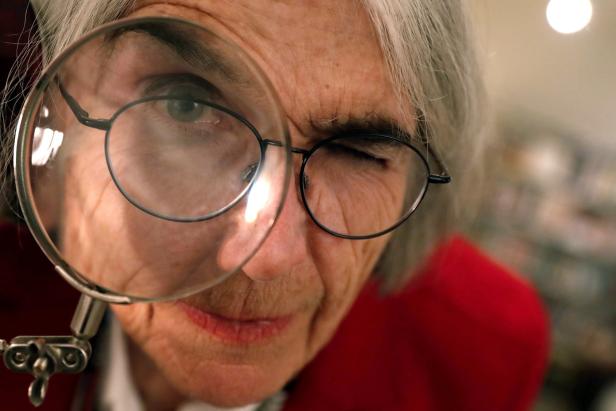 Eine ältere Frau mit Brille betrachtet etwas durch eine Lupe.