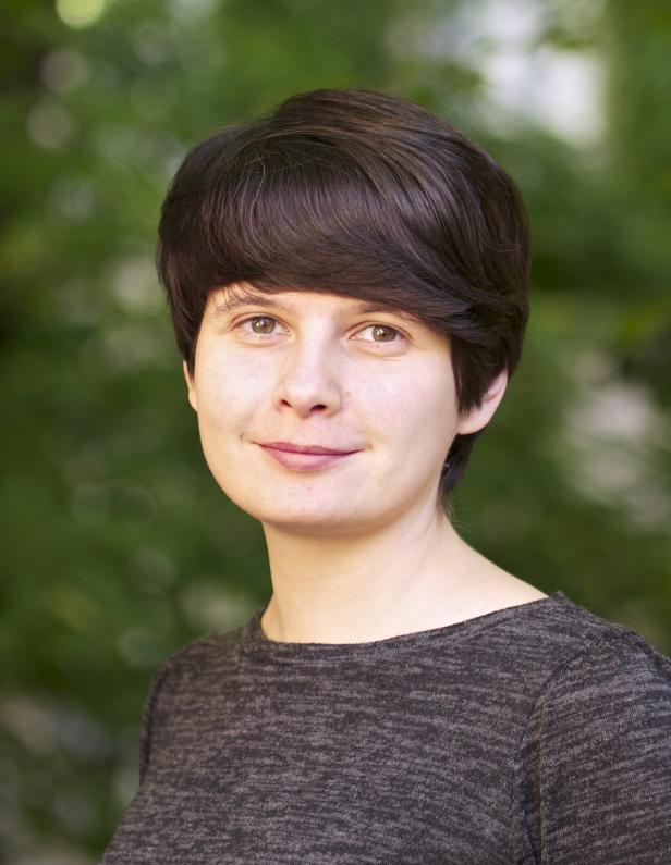 Anastasiya Yarovenko Eine Frau mit braunen Haaren und einem grauen Oberteil lächelt in die Kamera.