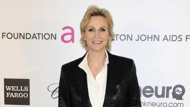 Jane Lynch posiert vor einem Hintergrund der Elton John AIDS Foundation.