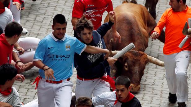 Beim Stiertreiben in Pamplona rennen Menschen vor einem Stier her.