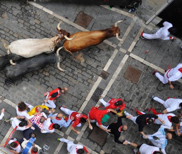 Draufsicht auf die Stierhatz von Pamplona mit rennenden Menschen und Stieren.
