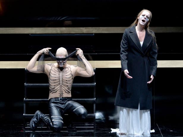 Ein Mann mit Skelettbemalung und eine Frau in einem schwarzen Mantel stehen auf einer Bühne.