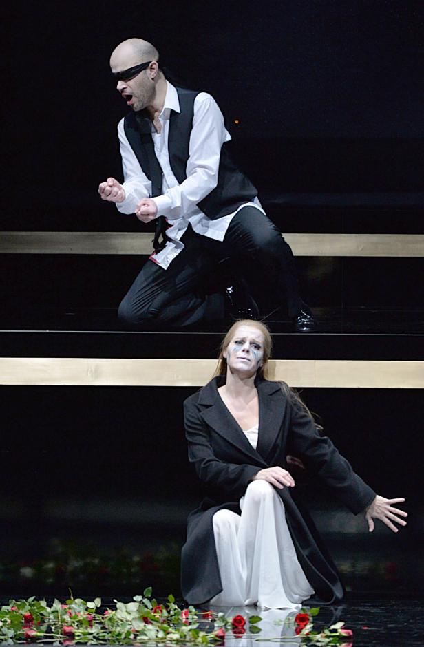 Ein Mann mit Augenbinde kniet über einer Frau auf einer Bühne mit Rosen.