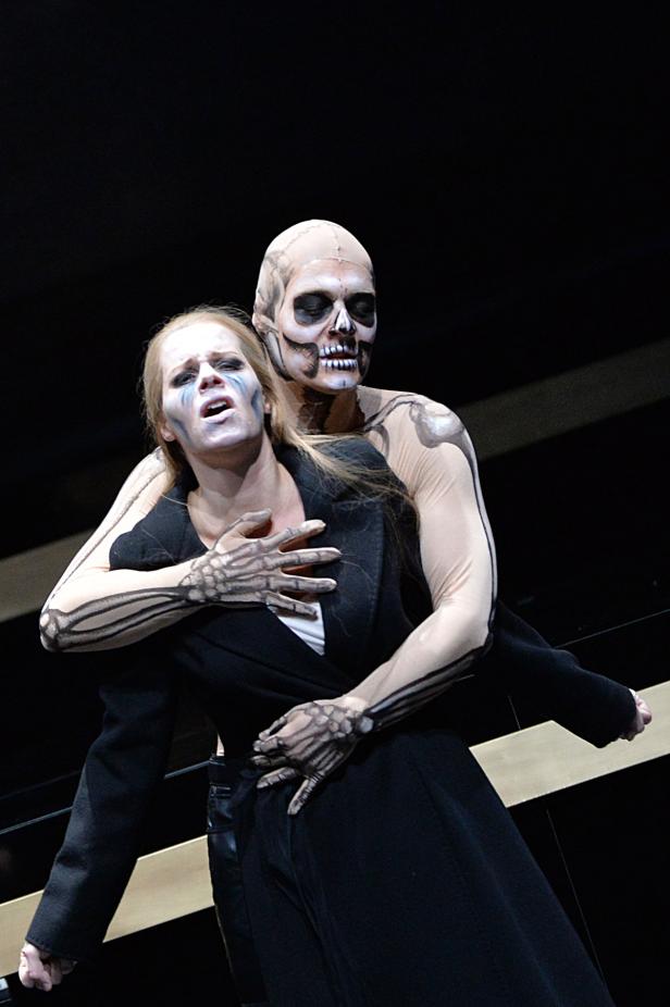 Eine Frau in einem schwarzen Kostüm wird von einer Person mit Skelett-Make-up umarmt.