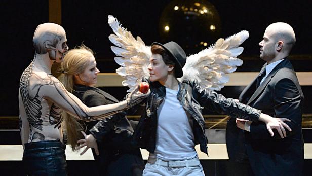 Eine Theaterszene mit einem Mann im Skelettanzug, einer Frau mit Apfel, einer Frau und einem Mann im Anzug.