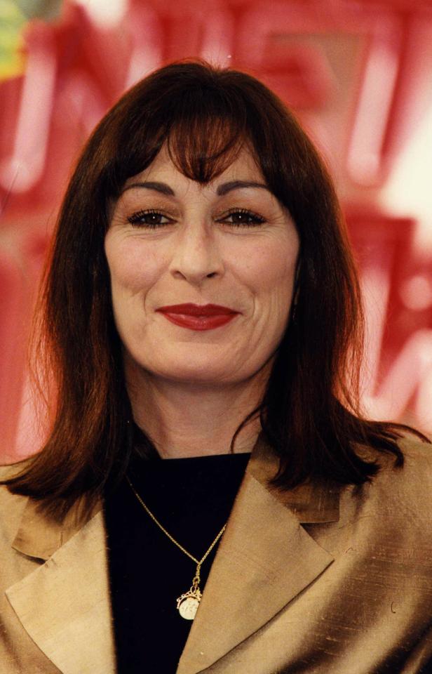Anjelica Huston mit rotem Lippenstift und goldener Jacke vor rotem Hintergrund.