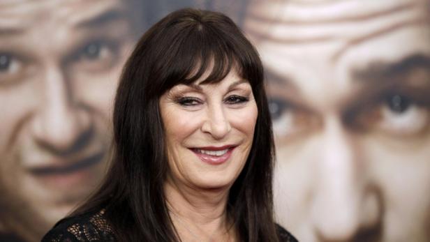 Ein Porträt der lächelnden Anjelica Huston vor einem verschwommenen Hintergrund.