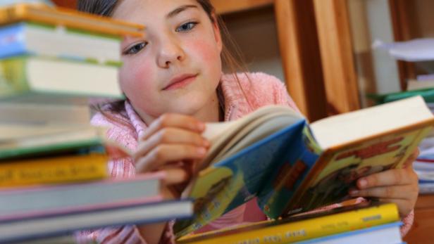 Ein junges Mädchen liest ein Buch inmitten eines Bücherstapels.