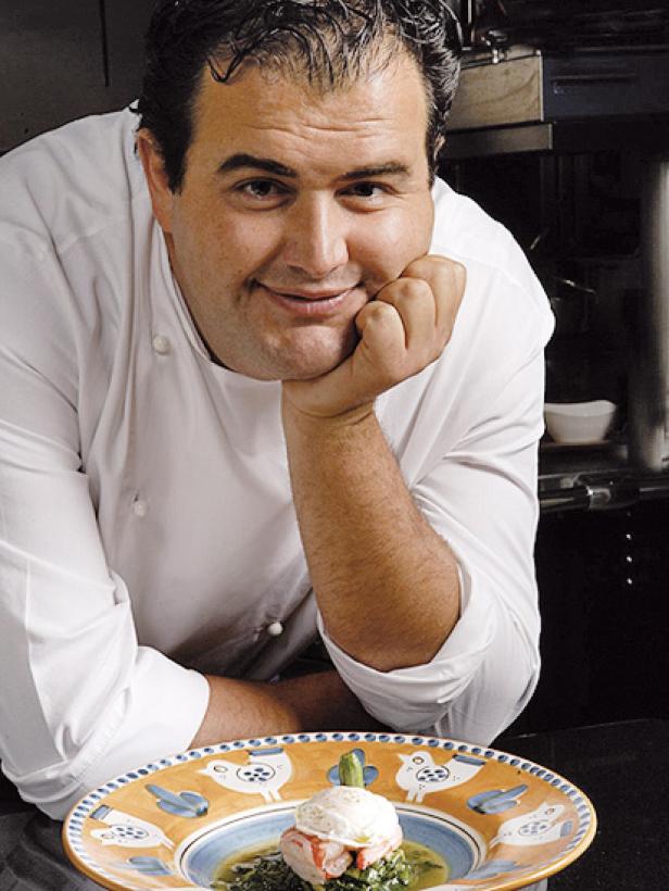 Ein Koch in Kochuniform präsentiert ein Gericht mit pochiertem Ei auf einem Teller.