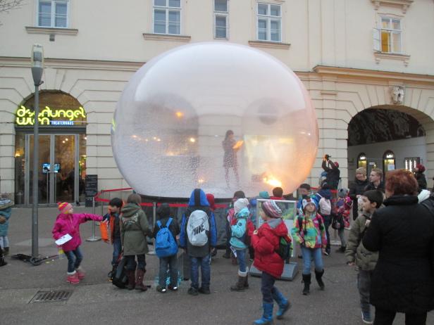 Eine Gruppe Kinder steht vor einer großen Schneekugel vor dem Theaterhaus Dschungel Wien.