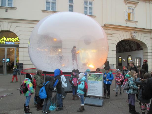 Eine Gruppe von Kindern steht vor einer großen Schneekugel vor dem Dschungel Wien Theaterhaus.