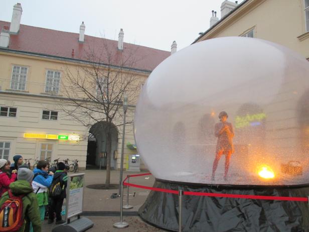 Eine Frau steht in einer riesigen Schneekugel, umgeben von Zuschauern.