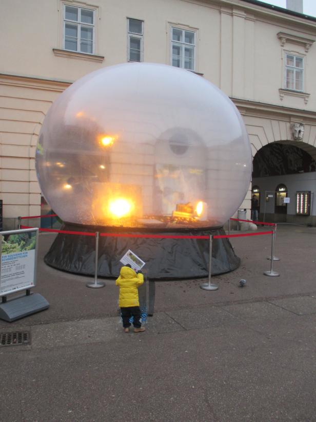 Ein Kind betrachtet eine übergroße Schneekugel mit einer Szene darin.