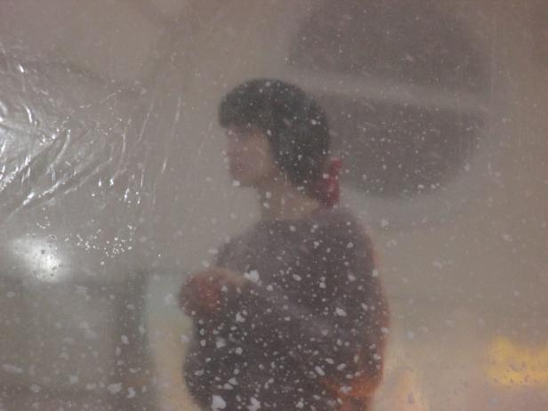 Eine verschwommene Person steht hinter einer transparenten, befeuchteten Oberfläche.