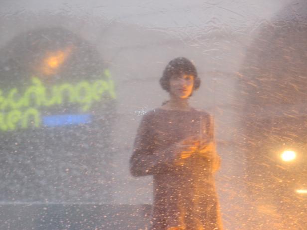 Eine verschwommene Aufnahme einer Person mit Kopfhörern vor einer beleuchteten Wand.