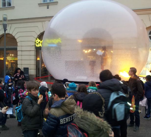 Eine Gruppe von Kindern steht vor einer großen, transparenten Schneekugel.