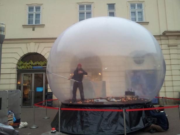 Eine Person putzt das Innere einer großen, transparenten Kugel vor dem Dschungel Wien Theaterhaus.