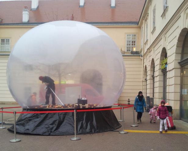 Eine Person reinigt das Innere einer riesigen Schneekugel, während eine Familie vorbeigeht.
