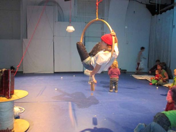 Eine Person mit roter Mütze hängt an einem Trapezring, während Kinder zusehen.