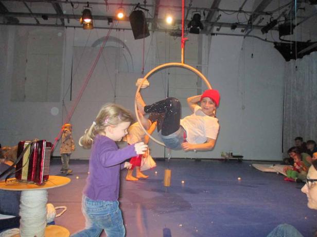 Eine Frau hängt in einem Reifen von der Decke, während ein junges Mädchen zusieht.