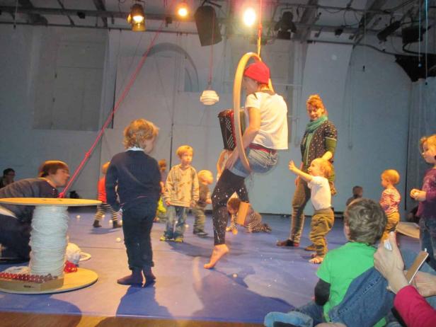 Eine Frau hängt in einem Reifen von der Decke, umringt von Kindern.