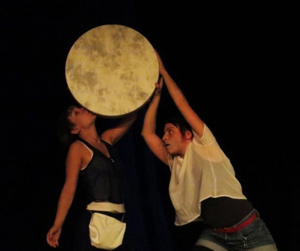 Zwei Personen halten eine große Rahmentrommel hoch, eine küsst sie.