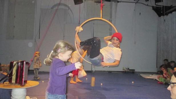 Ein Mädchen steht vor einer Frau, die in einem Reifen hängt, während Zuschauer zusehen.