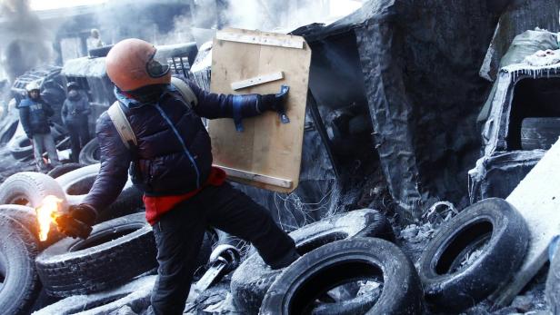 Ein Demonstrant mit Helm und Schild steht auf einem Reifenstapel und hält einen Molotowcocktail.