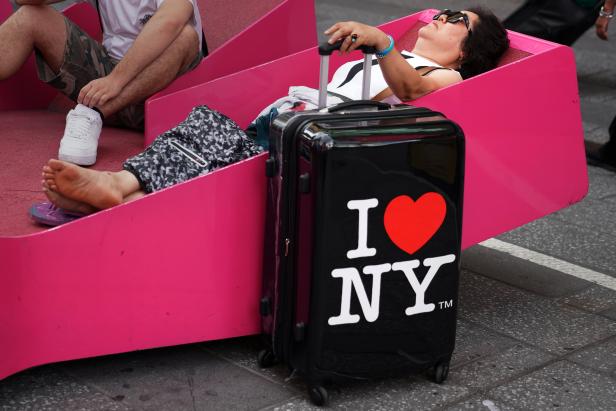 A woman takes a nap on a bench as she holds onto an I Love New York suitcase in Times Square in the Manhattan borough of New York City