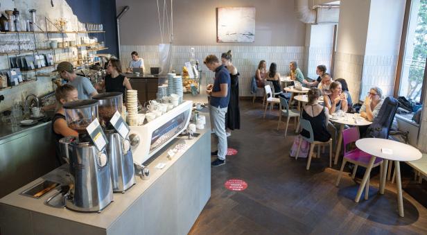 In einem belebten Café sitzen und arbeiten Menschen an Tischen und an der Theke.