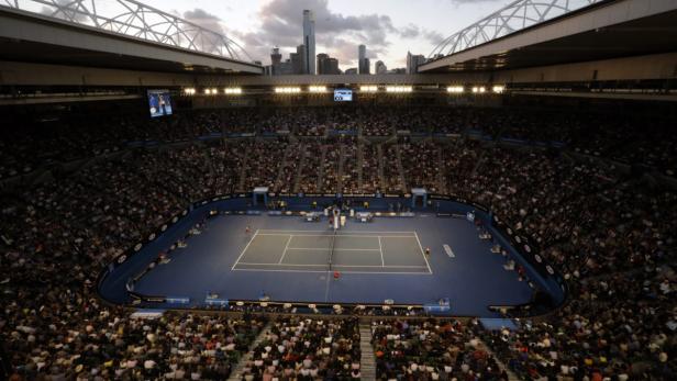 Blick auf ein Tennismatch in einem vollbesetzten Stadion mit der Skyline von Melbourne im Hintergrund.