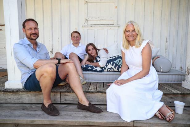 Kronprinz Haakon, Kronprinzessin Mette-Marit und ihre Kinder sitzen vor einem Holzhaus.
