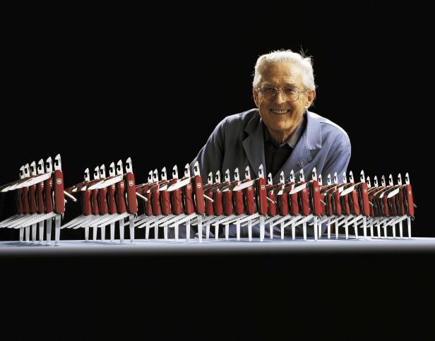 Ein älterer Mann lächelt hinter einer Reihe von Schweizer Taschenmessern.