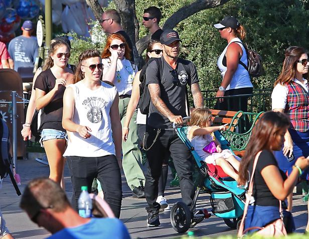 David Beckham schiebt seine Tochter in einem Kinderwagen, während sie von anderen Personen umgeben sind.